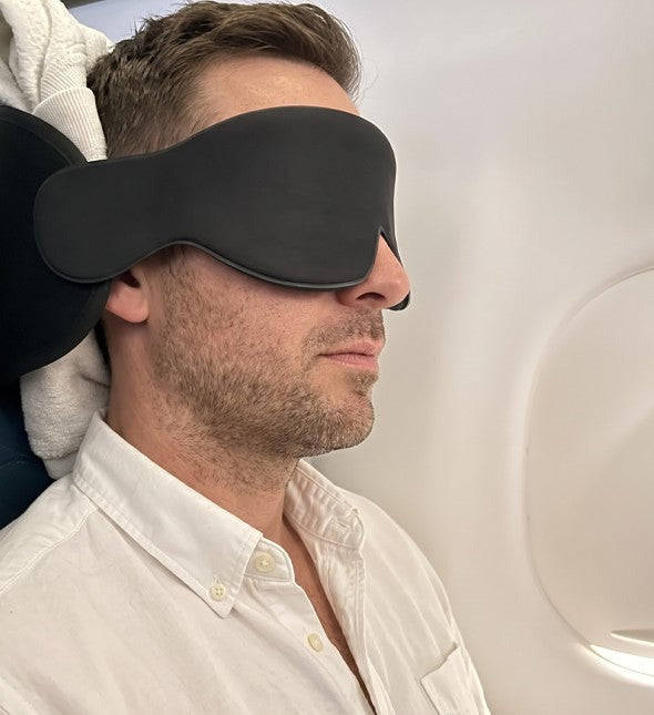 Traveler asleep in a window seat with the JetNod band and mask
